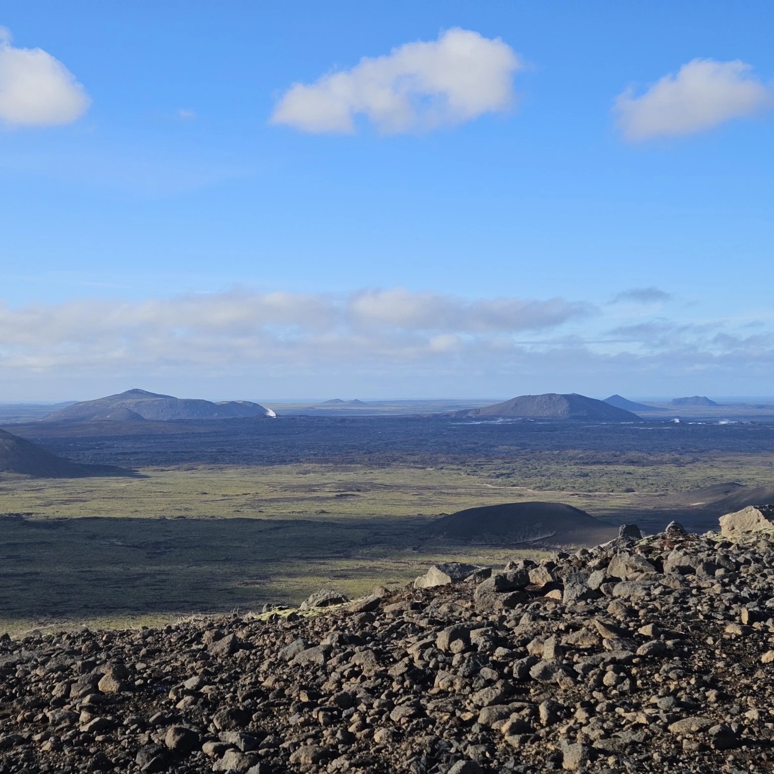 A wide volcanic landscape of dark lava fields and low craters seen from the Fagradalsfjall hiking area