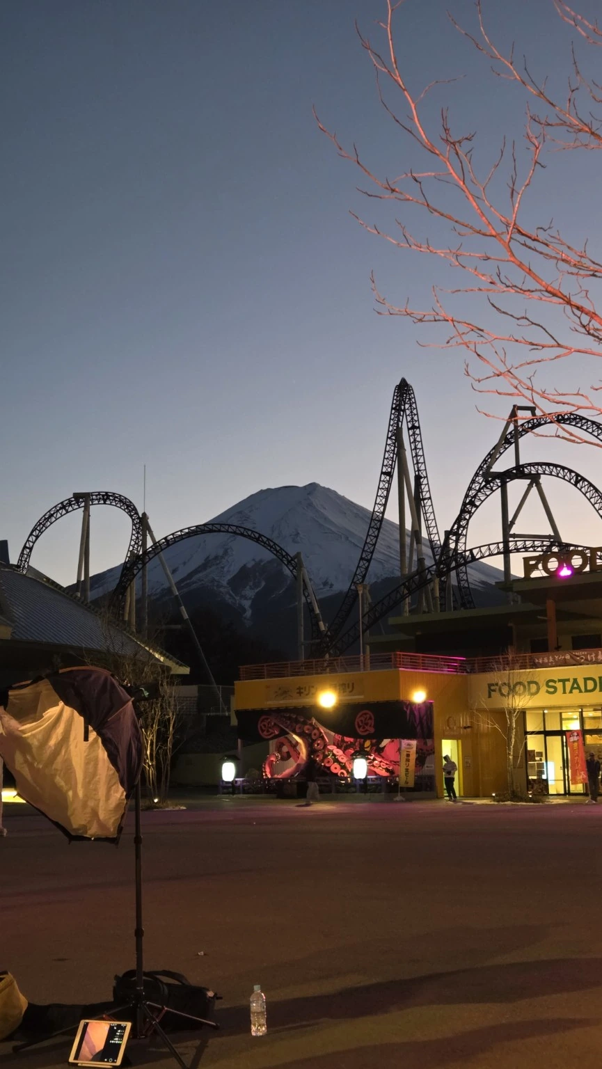 Mount Fuji framed by roller-coaster tracks around dusk at Fuji-Q Highland