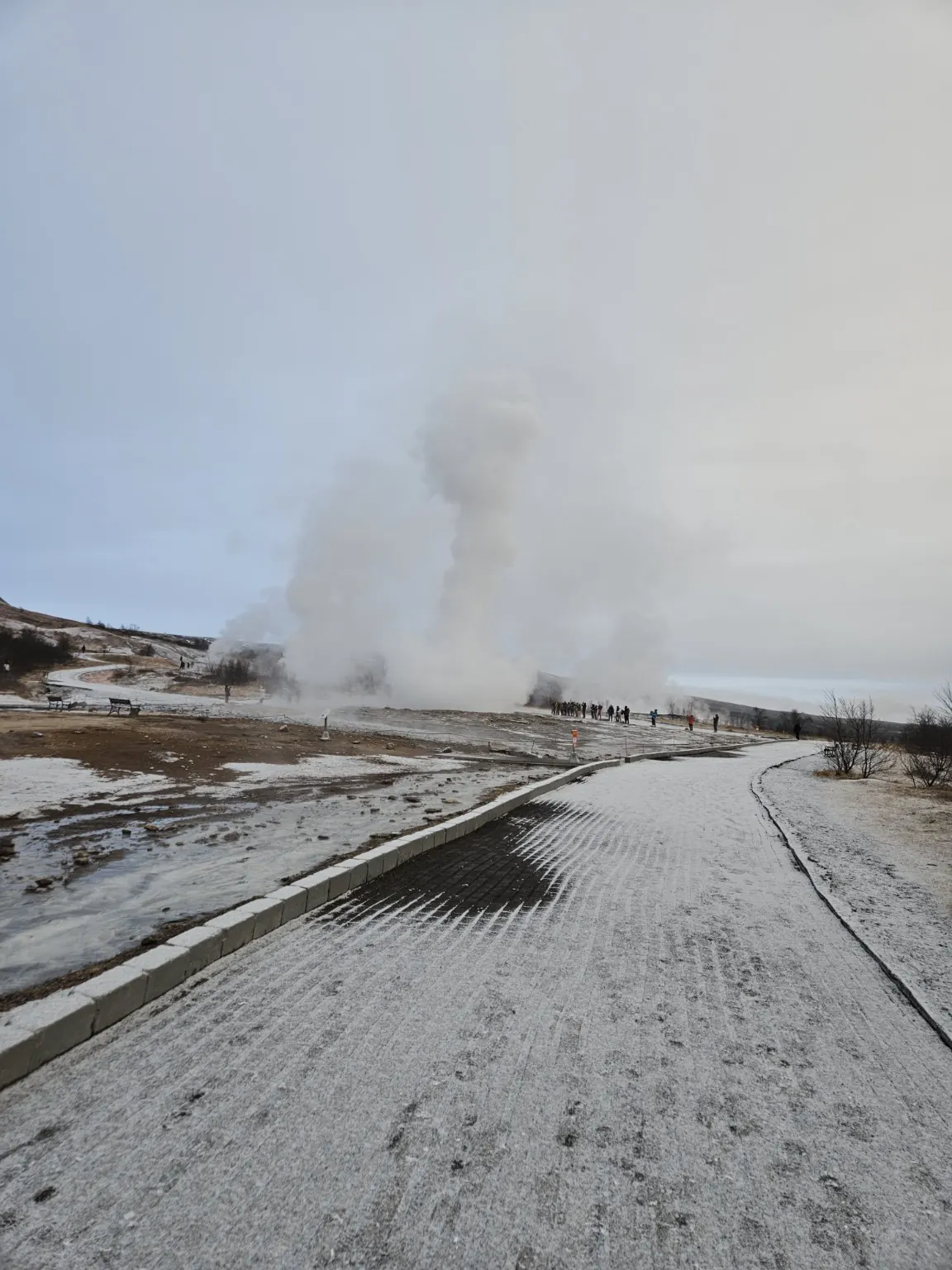 Visitors watching a huge column of steam rise from Strokkur across the lightly snow-covered Geysir geothermal area