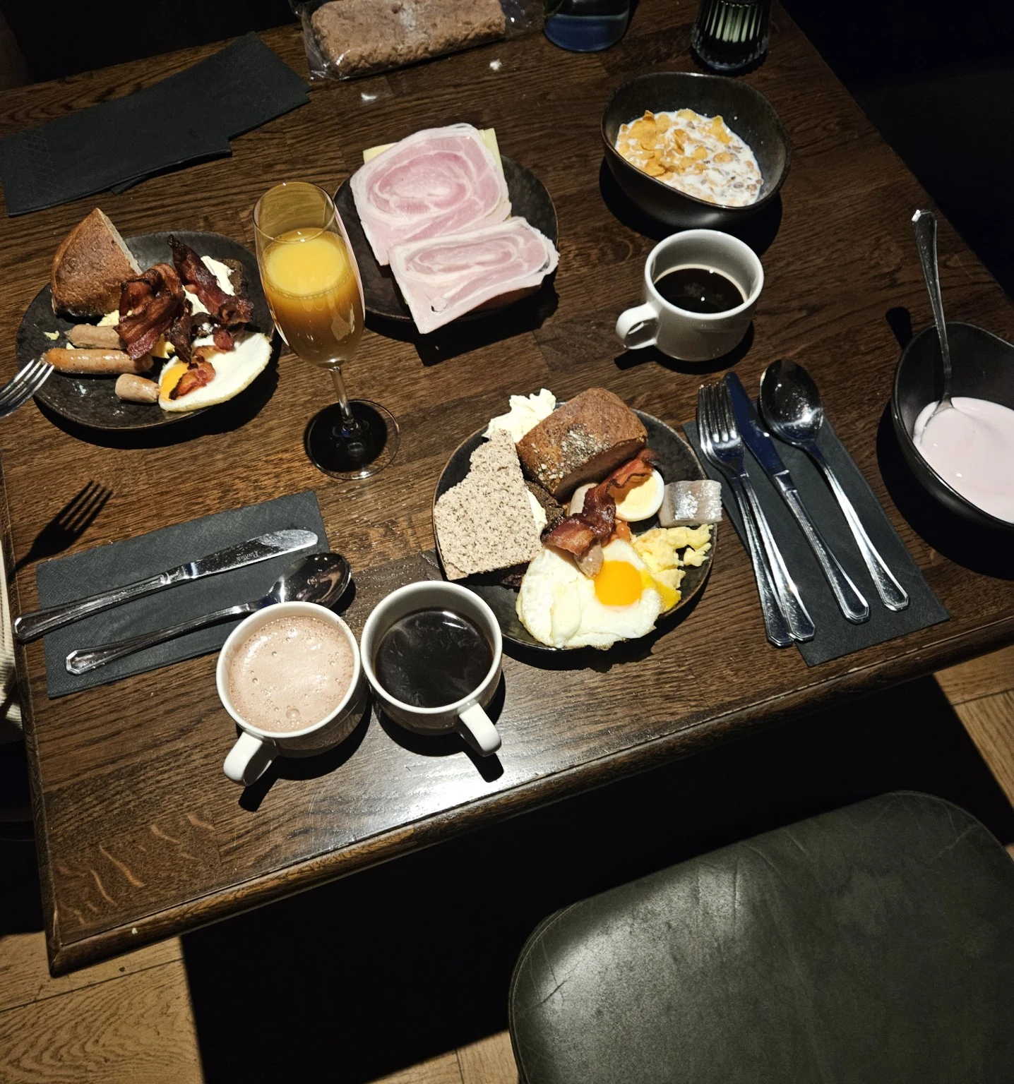 A substantial breakfast plate with eggs, bacon, ham, bread and drinks