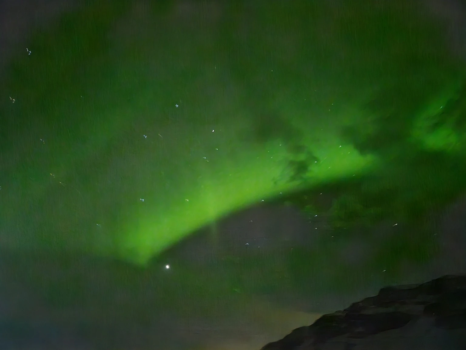 A bright green aurora stretching across the dark sky near Kvíhólmi Premium Apartments