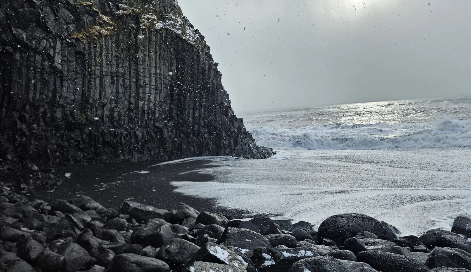 Heavy white surf next to towering basalt cliffs at Reynisfjara black sand beach in winter