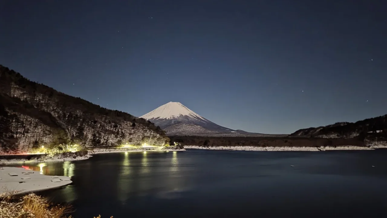 Snow-covered Mount Fuji across Lake Shoji on a winter night from Shoji Lake Hotel