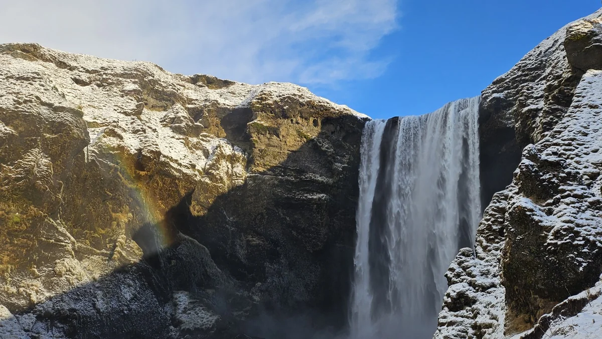 A rainbow beside Skógafoss as the waterfall drops through snow-covered cliffs in winter