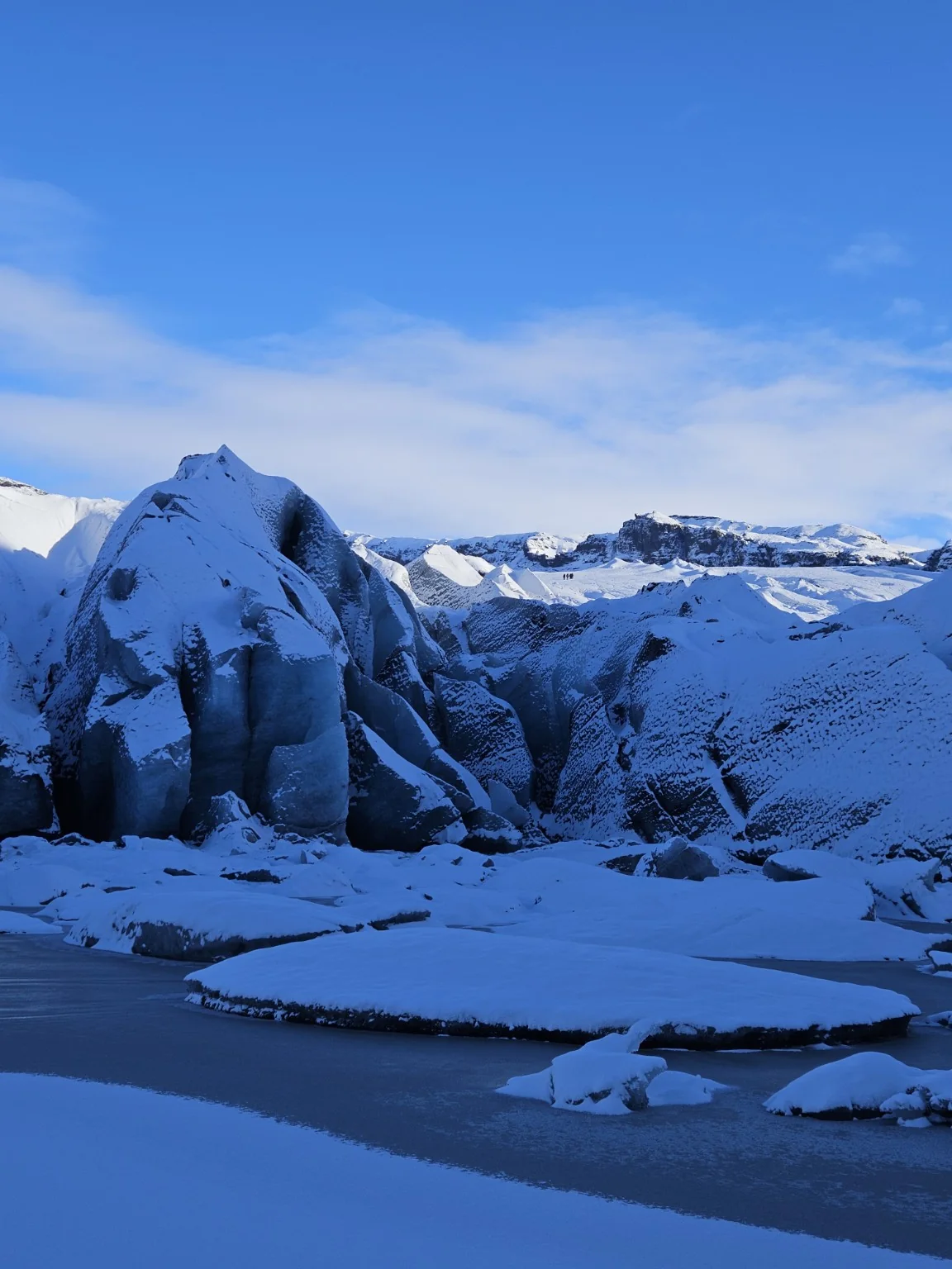 Snow and dark volcanic debris layered across the blue winter ice of Sólheimajökull