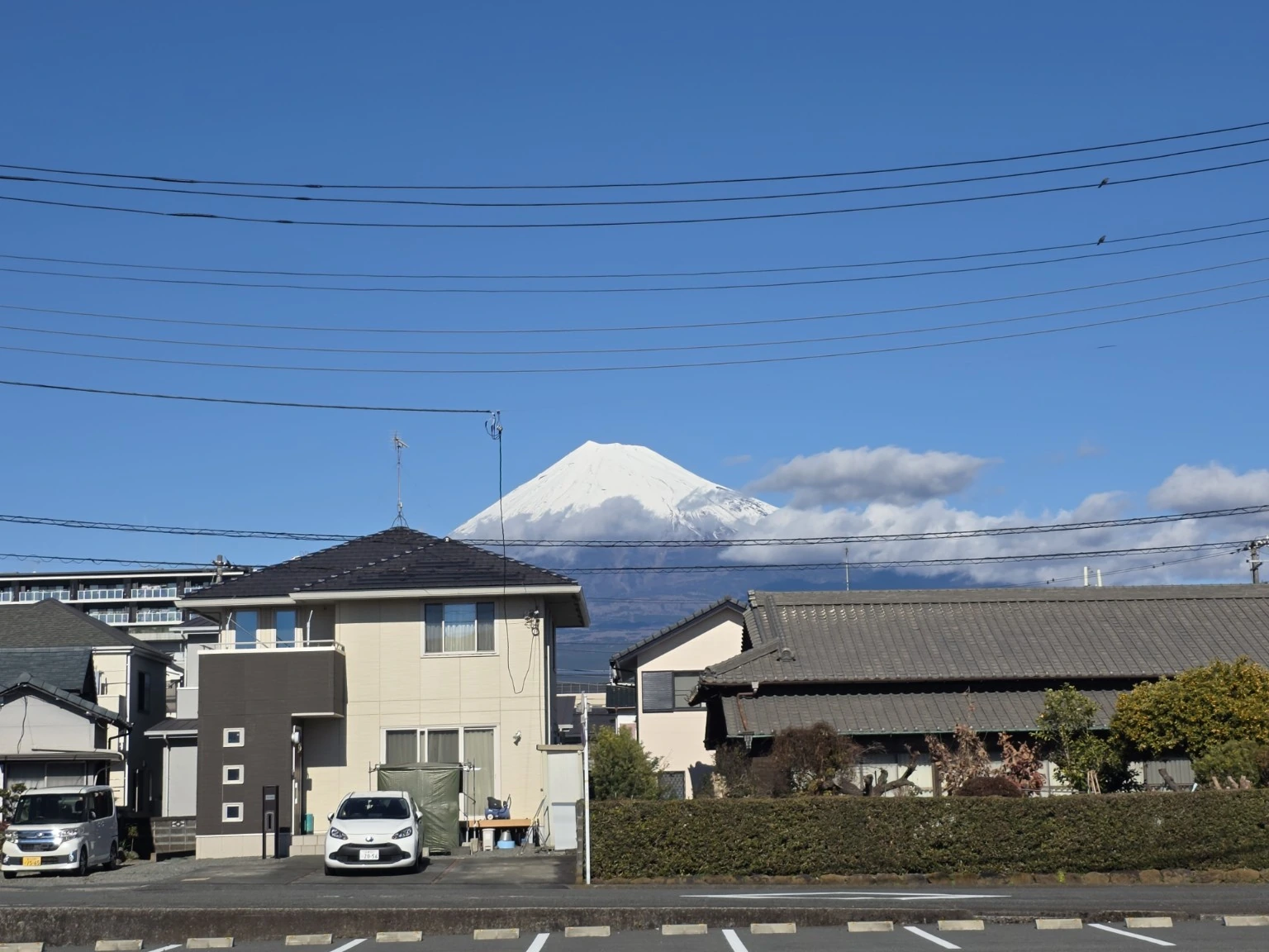 Snow-covered Mount Fuji behind a small river and residential neighborhood near Yanagida Bridge in Fuji
